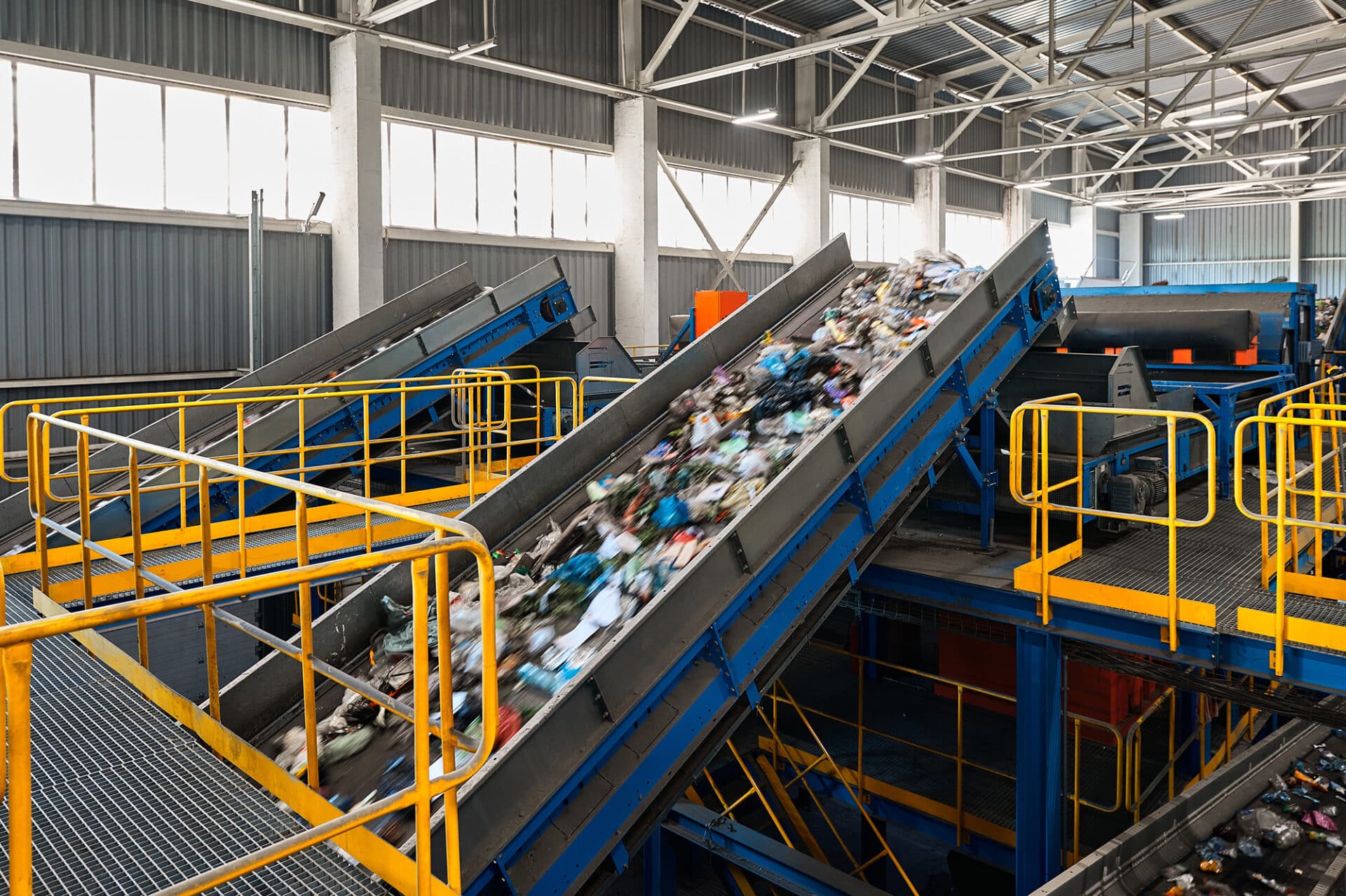 A large industrial conveyor belt system with blue and yellow railings, transporting waste materials.