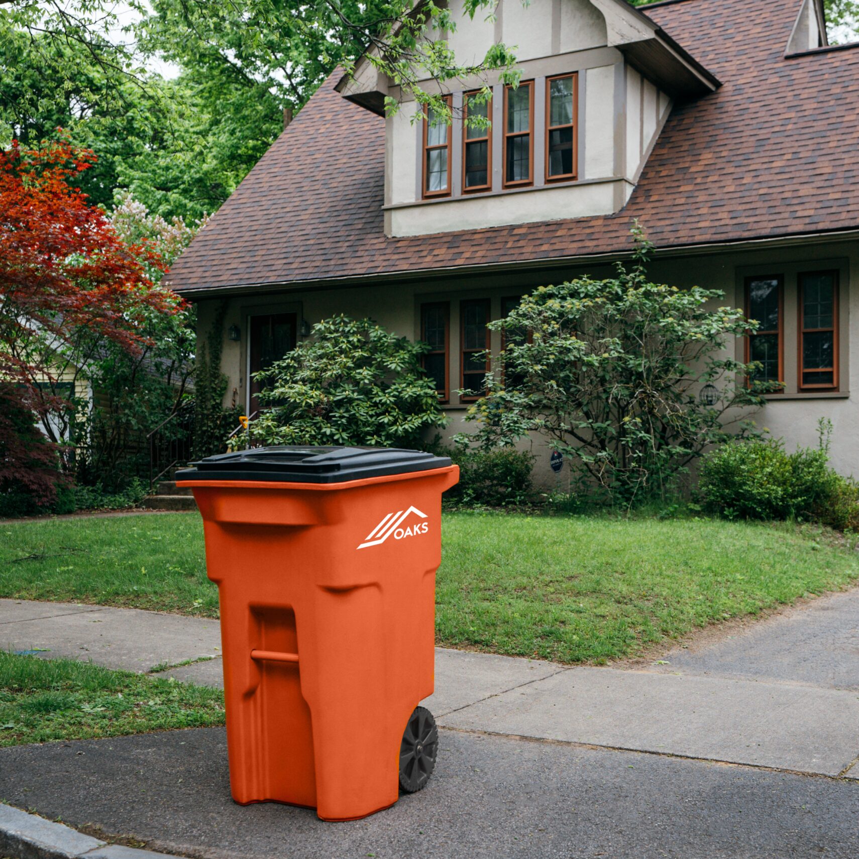An orange trash can on a residential street. The can is awaiting pickup.