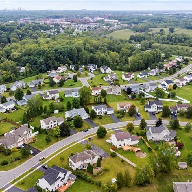 a suburban neighborhood with many houses and green lawns. The houses are mostly one-story and have gray roofs.